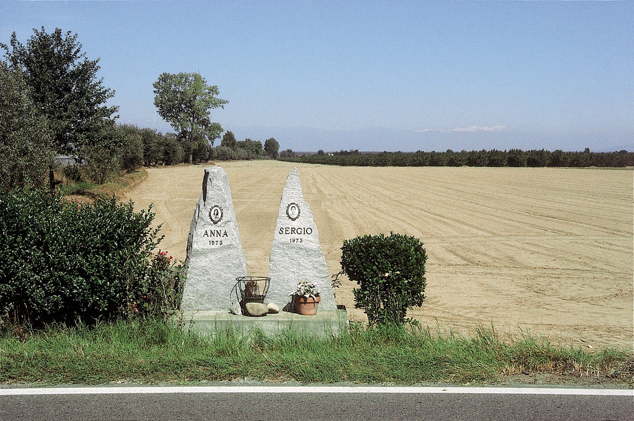 Photograph of two jagged gravestones placed on a grass verge beside a road with a bare field behind