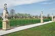 Photograph of a path with three statues on podiums, the path cutting through grass divided by a wire fence