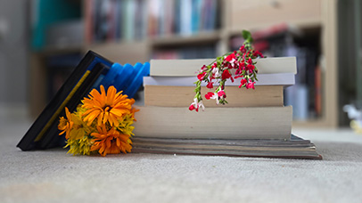A stack of magazines and books with flowers laid on top and to the side, laid on carpet on the floor of a room
