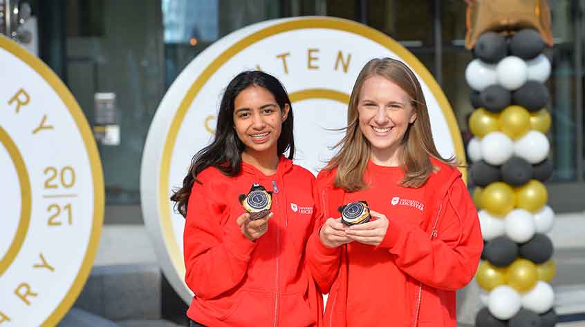 4/10/2021 - 2 students in red hoodies enjoying cupcakes as part of the University's centenary celebrations