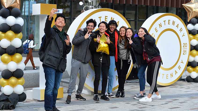 4/10/21 - a group of students take a selfie in front of our Big 100 on campus for our centenary