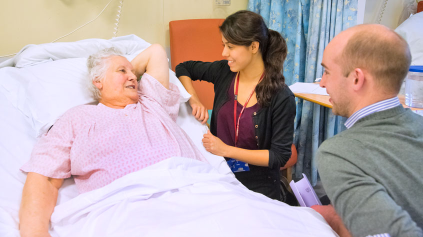 Two healthcare professionals talking to a patient in a bed.