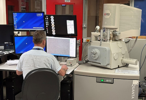 A researcher sitting in front of four screens attached to the SEM using the EDS technique