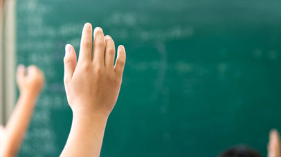 Hands raised in a classroom with a blackboard as background.