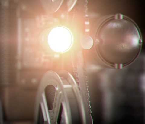 Movie projector with light beam and film reels on dark background