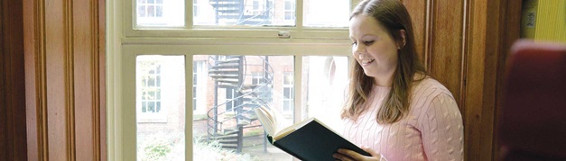 student sat reading by a window in an old library