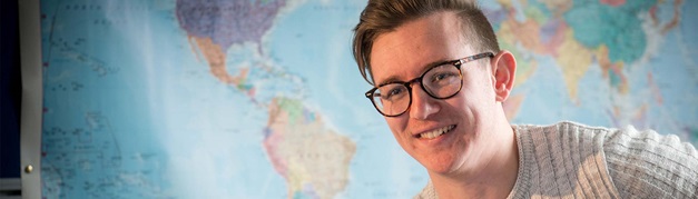 student smiling with a map of the world behind