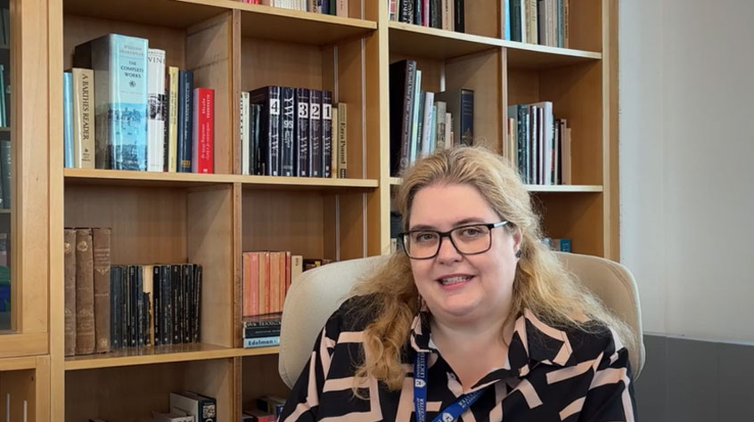Lecturer talking to camera with a shelf full of books behind her.