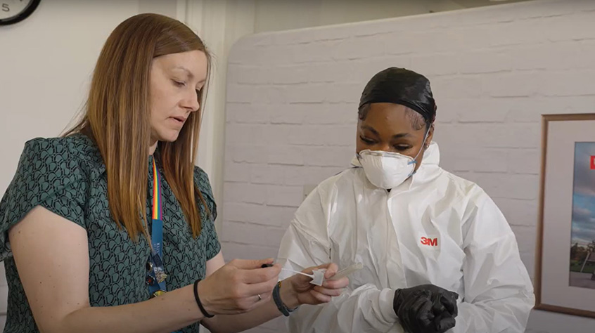 Teacher and student discussing a crime scene, student is dressed in protective clothing.