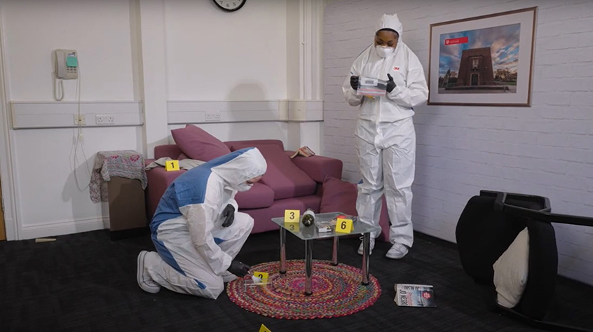 Two students looking around a crime scene set up as part of criminology's facilities