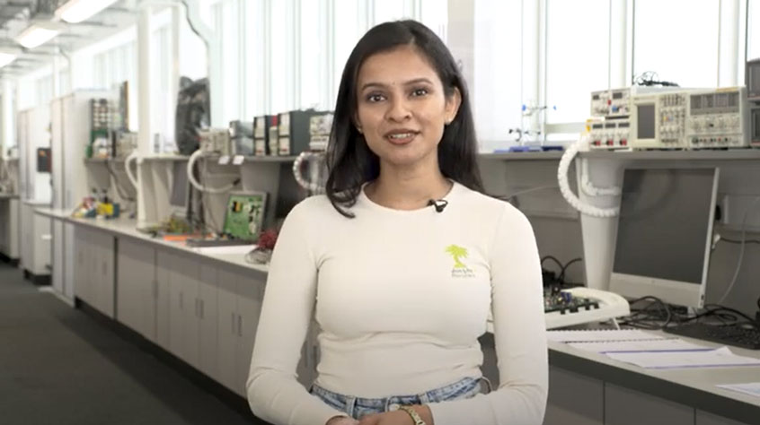 Student smiling to the camera whilst standing in an engineering lab.