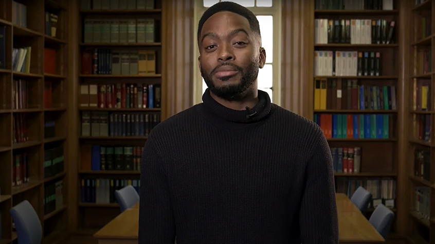 A Leicester law student sat within one of the rooms within Leicester Law school, bookshelves full of books sat behind.