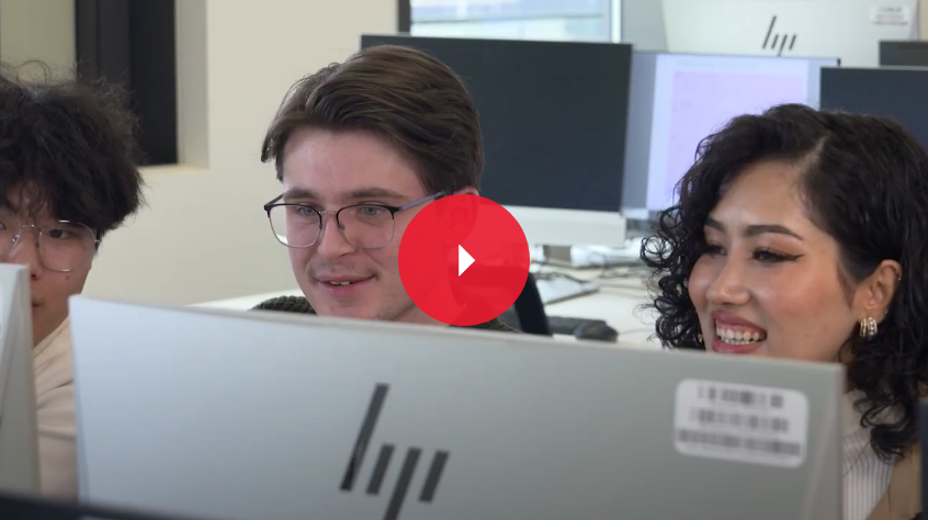 three students look at a computer, they smile amongst each other 