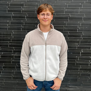 Student standing in front of a brick wall, wearing a fleece.