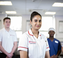 female nurse smiling and two male healthcare professionals stood behind