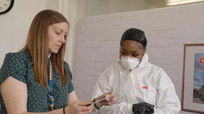 Two women looking at a swab. One of them is wearing full PPE.