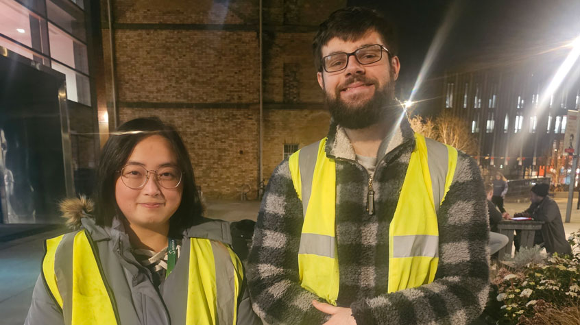 Two people wearing hi-vis jackets and smiling at the camera.