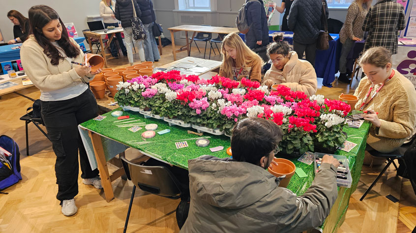 People working on painting flower pots around a large table.