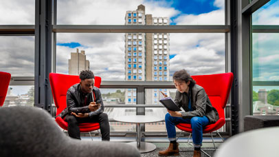 Two students, sitting on large chairs and looking at their phones.
