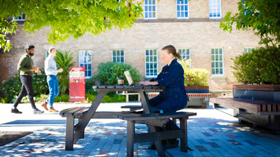 A student sitting on a bench on Leicester campus, working on a laptop
