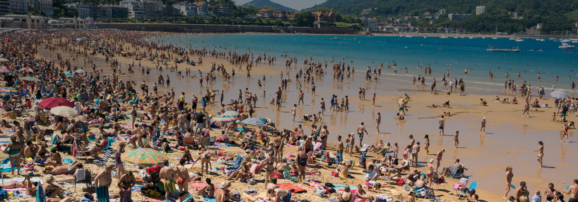 Hundreds of people on a beach, with sand and blue water.