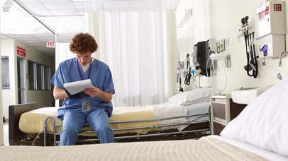 Medical student, sat on a hospital bed, writing some notes.