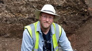 Mathew Morris sitting in a hole at a dig site