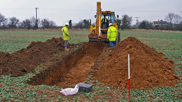 Archaeologists standing in front of a digger and near freshly dug earth