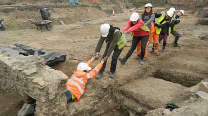 Group of archaeologists helping to pull a colleague out of a hole on an excavation site.