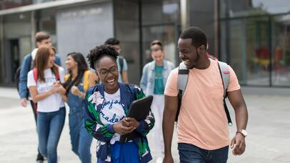Group of students chatting whilst walking towards camera and with David Wilson Library in the background