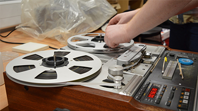 A photo of someone's hands changing an old large reel audio cassette