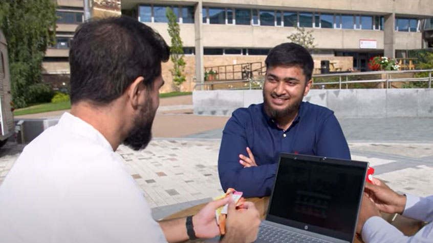 Medicine student Syed sitting in Centenary square on Leicester campus, talking to a friend.