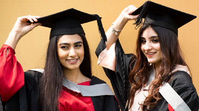 Two smiling graduates in academic gowns and mortarboard hats