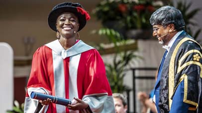 One Graduand looking on smiling and President and Vice-Chancellor Professor Nishan Canagarajah in De Montfort Hall