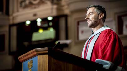 Man in robes giving a speech at the ceremony in De Montfort Hall
