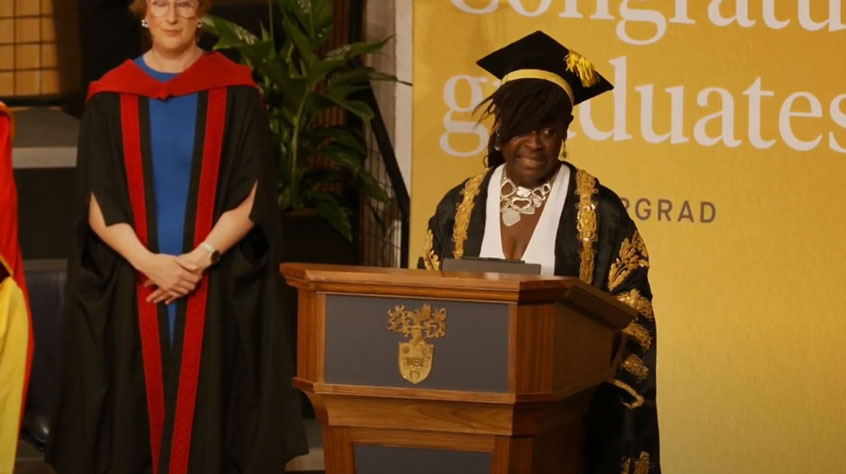 Maggie Aderin-Pocock standing at a lectern in graduation robes.