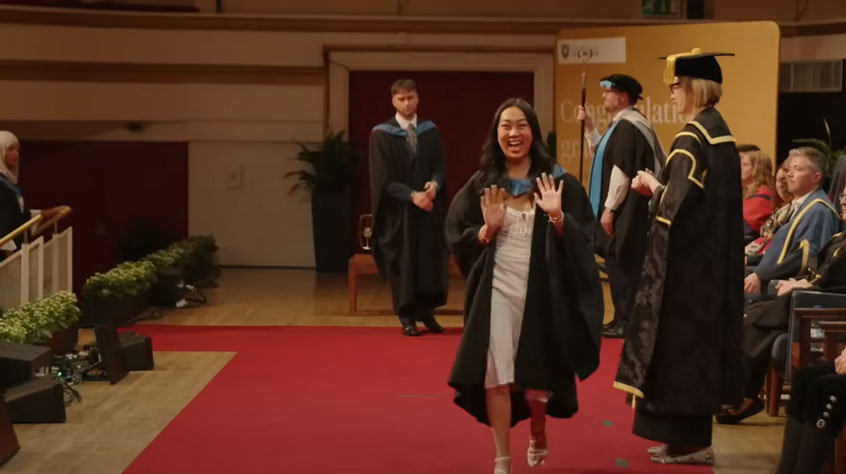 Student walking across a stage in graduation robes.