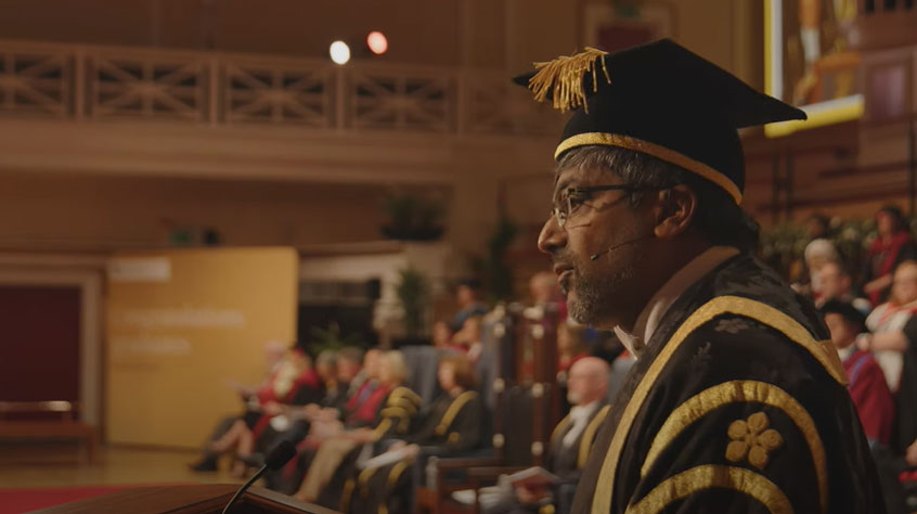 Nishan Canagarajah standing at a lectern in graduation robes.