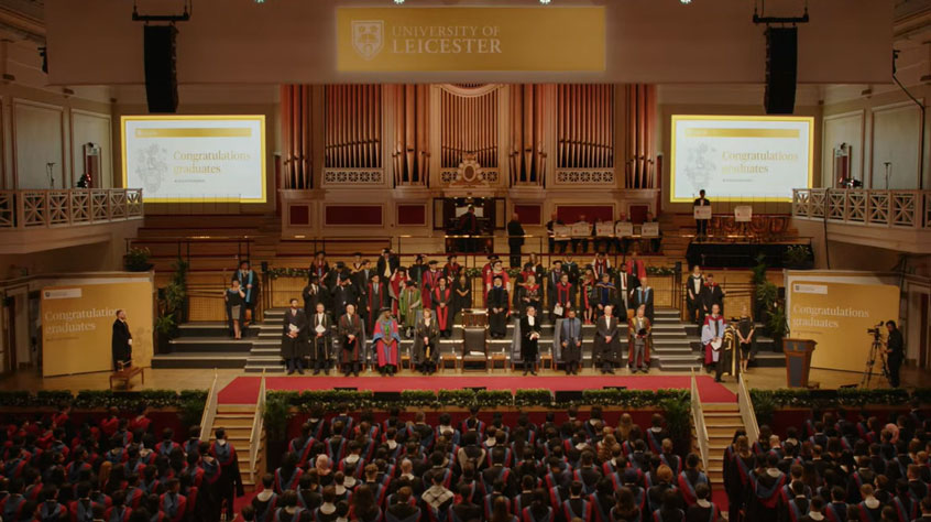 Wide shot of people standing on a big stage at graduation.