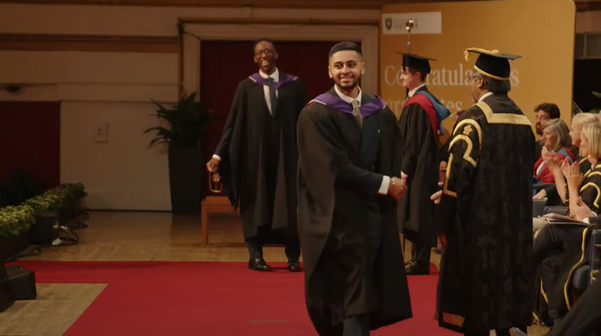 Graduate walking across a stage in graduation robes.