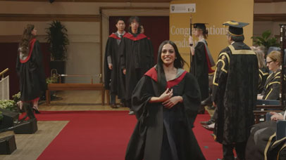 Student walking across a stage in a cap and gown, smiling at the camera