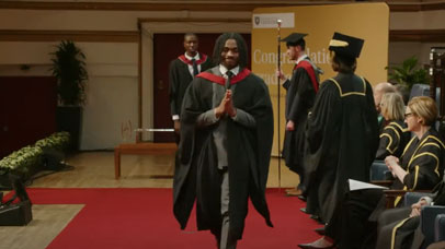 Student walking across a stage in a cap and gown, smiling at the camera