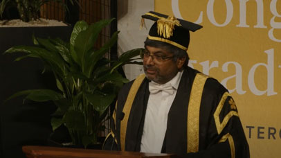 Professor Nishan Canagarajah speaking at graduation and wearing a cap and gown.