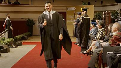 Student walking across the stage, giving the thumbs up to the canera