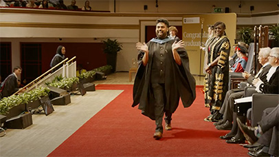 Student walking across the stage, smiling and waving at the camera