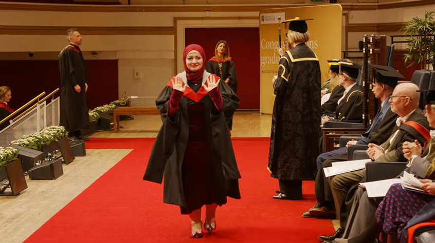 Female Graduand walking across the stage at DeMontfort Hall on the 4.30pm Graduation ceremony for the University of Leicester