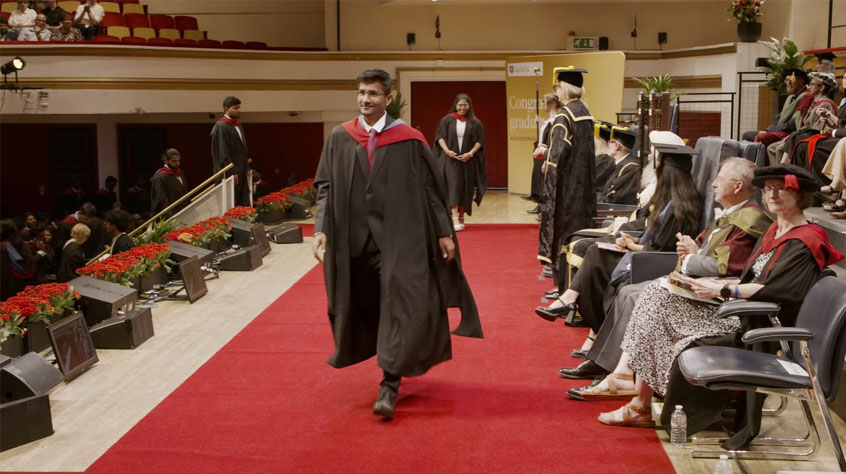 Male Graduand walking across the stage at DeMontfort Hall on the 1.30pm Graduation ceremony for the University of Leicester