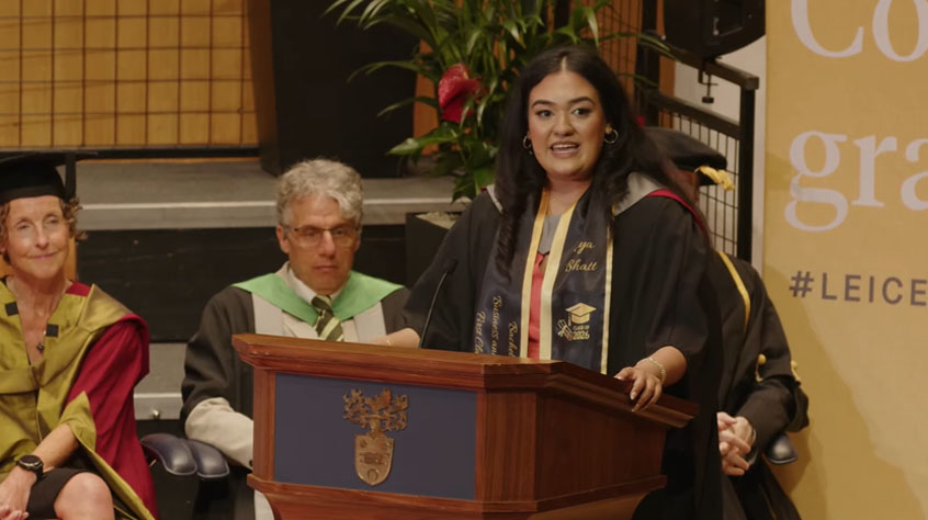 A woman dressed in a graduation gown giving a speech.