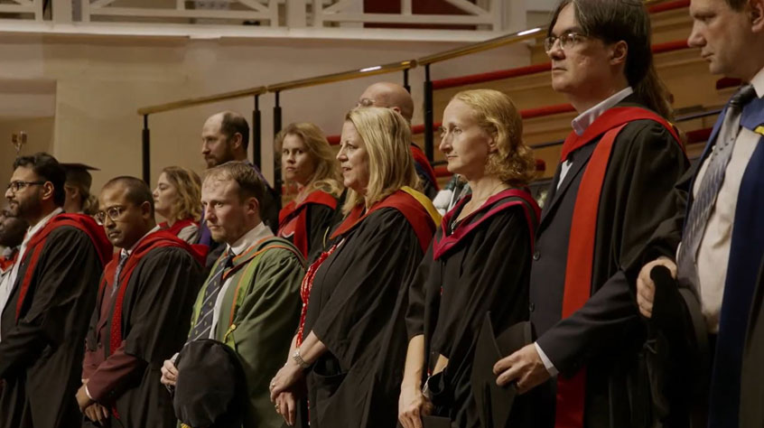 Students in graduation gowns standing in a line, singing.