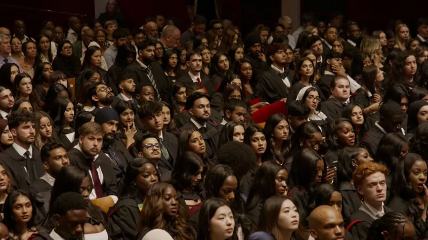 Hundreds of students sitting in their graduation gowns.
